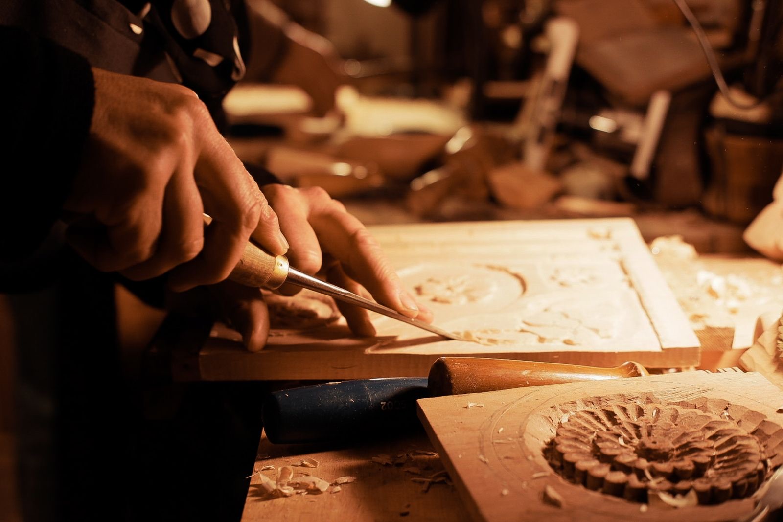 A craftsman's hands carving an intricate floral medallion into wood