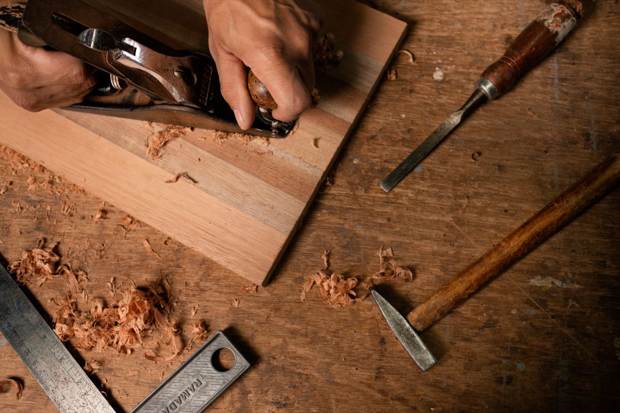 Hand tools, a freshly planed board and curls of shavings on a dark workbench
