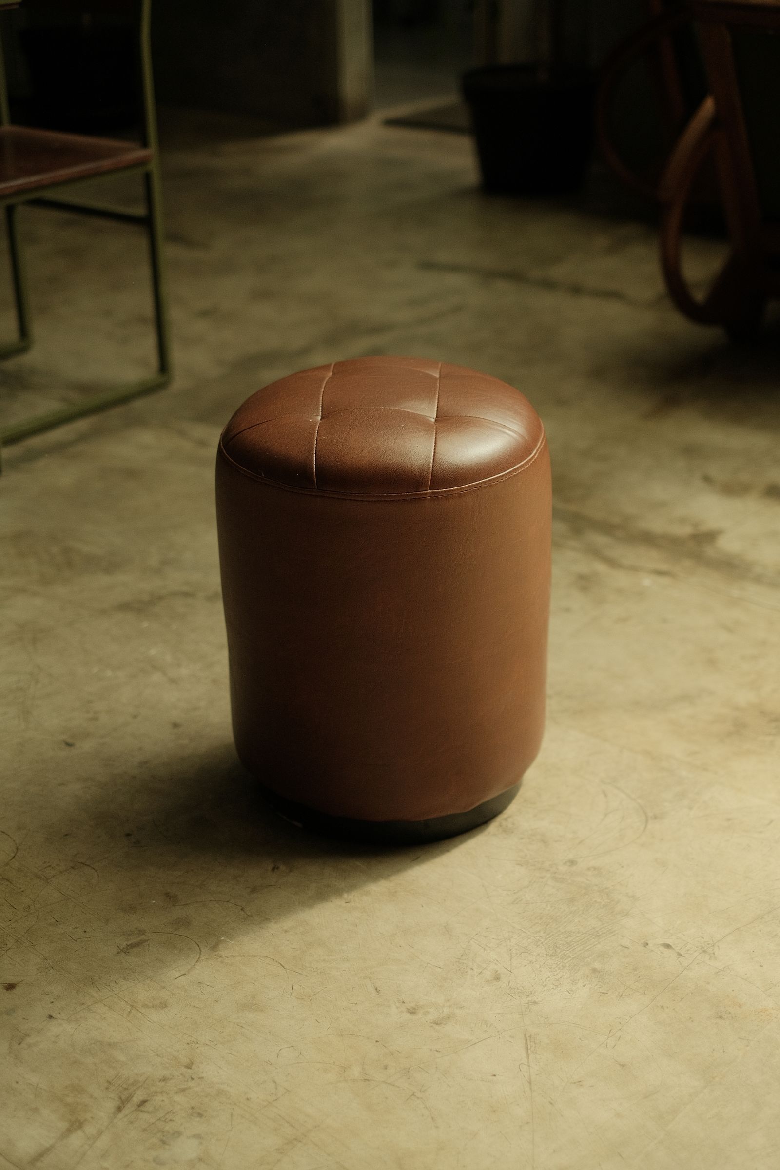 A drum ottoman with a stitched leather seat in low workshop light