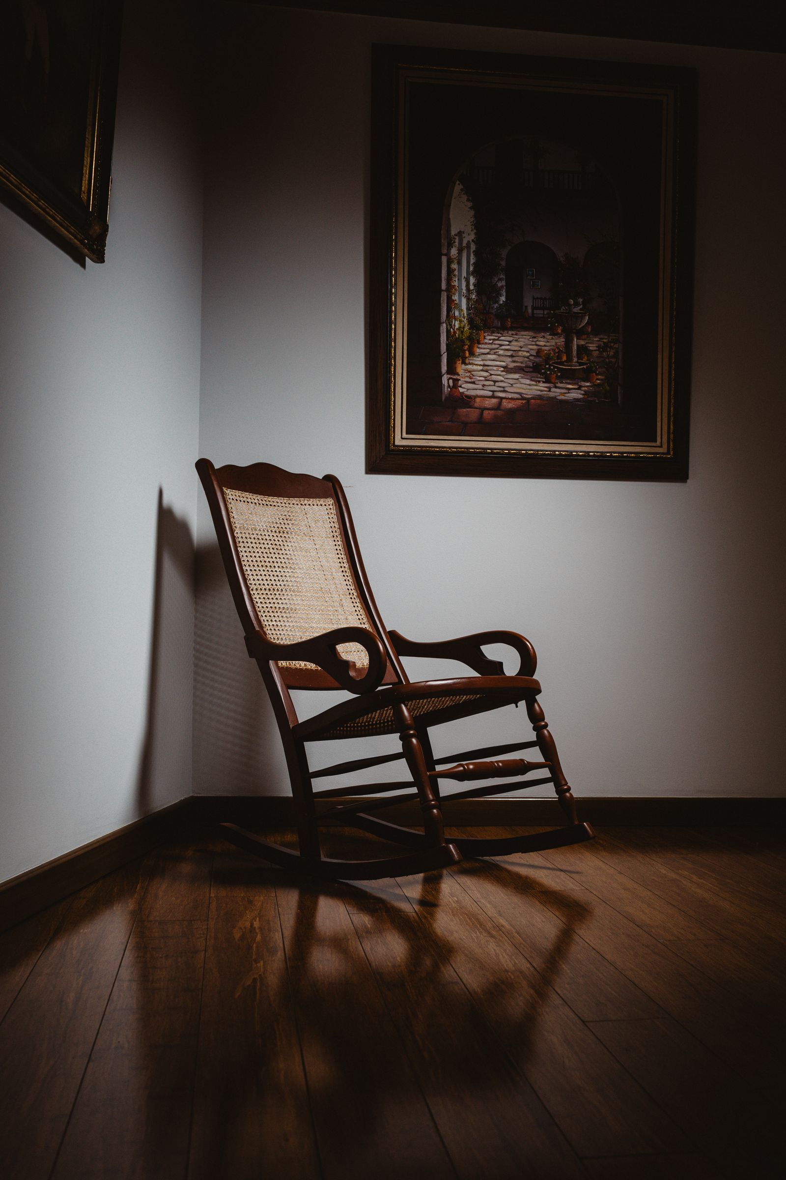 A caned walnut rocking chair resting in a pool of soft window light